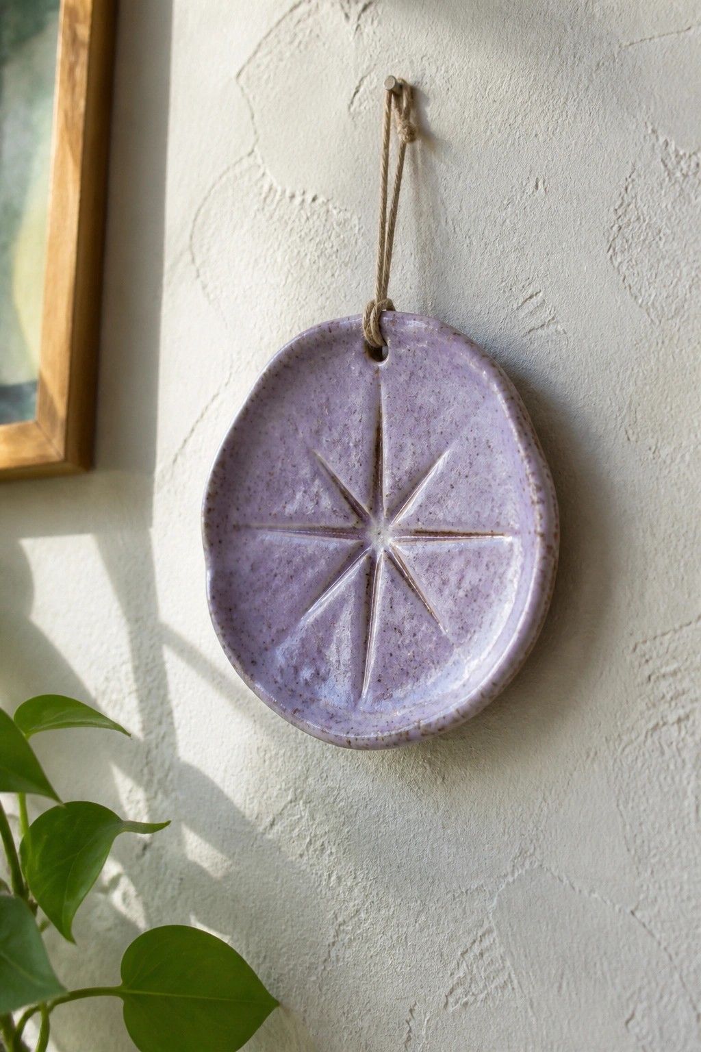 Purple ceramic dish with embossed starburst design hanging on textured wall by twine
