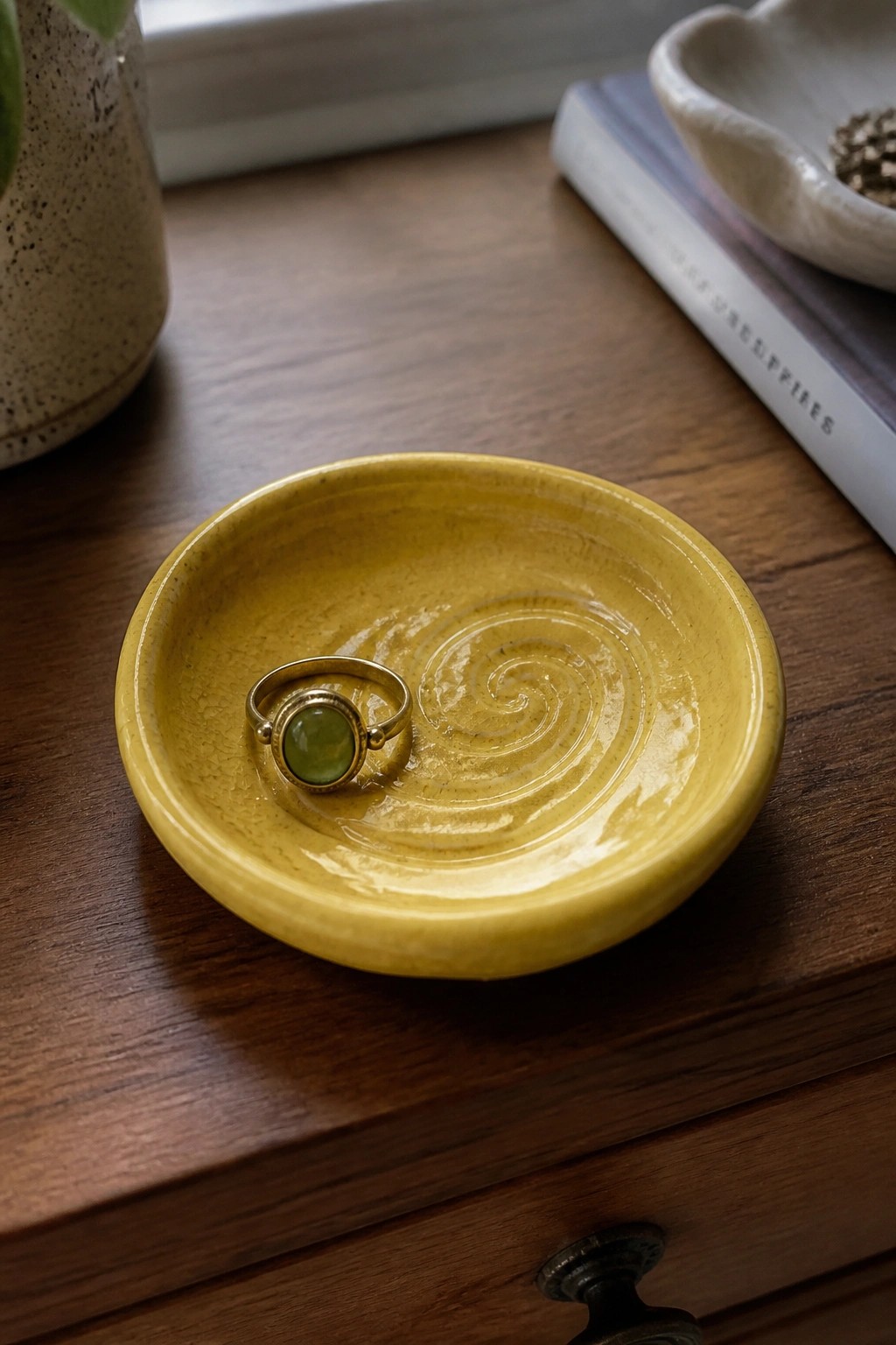 Gold ring with green stone in yellow swirled ceramic bowl on wood