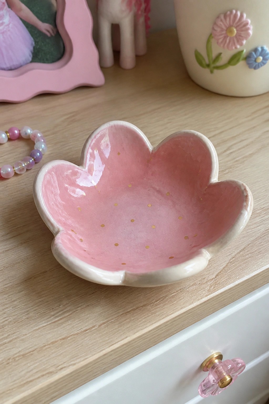 Pink flower-shaped ceramic bowl with gold dots on wooden dresser