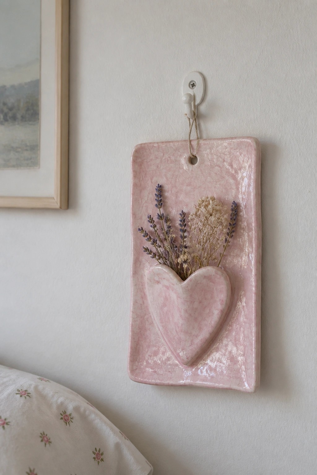 Pink ceramic tile with heart pocket of dried lavender hanging on white wall