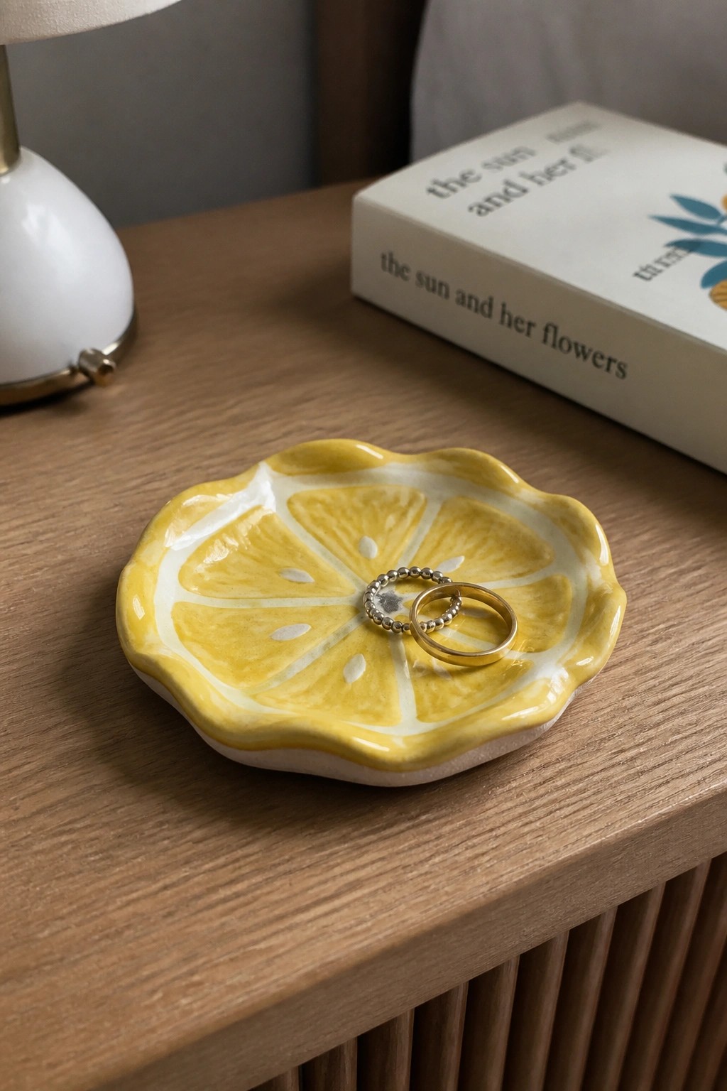 Yellow lemon-shaped ceramic dish holding two rings on wooden table beside book