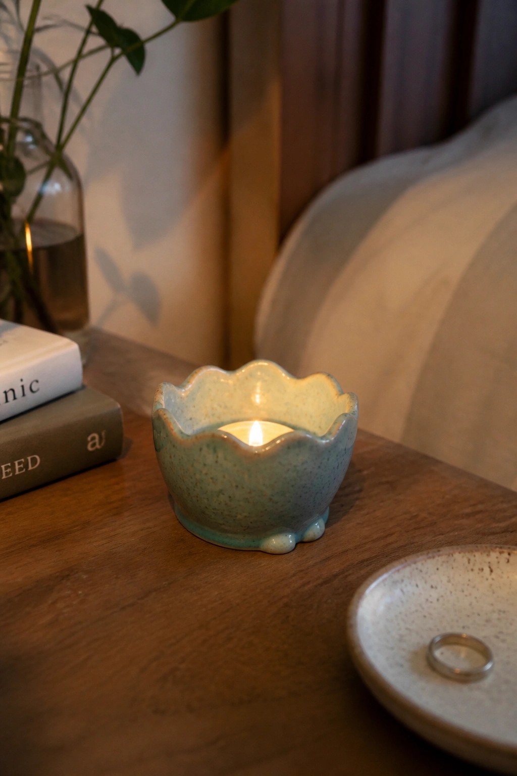A small blue-green ceramic bowl with a scalloped rim holds a lit tea light candle on a wooden table.