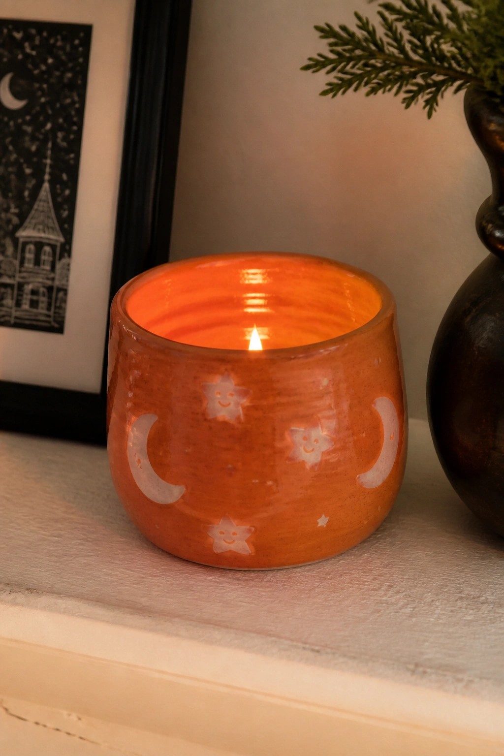 Lit orange ceramic holder with smiling stars and crescent moon cutouts on shelf