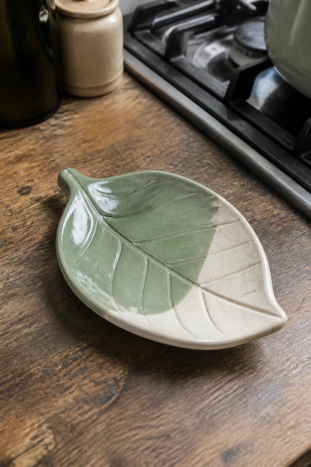 Ceramic leaf-shaped dish in green and beige on rustic wooden counter.