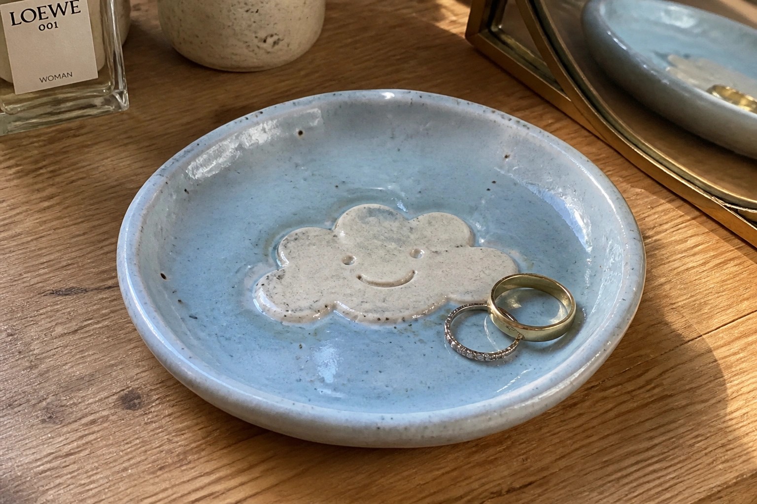 Blue ceramic dish with smiling cloud holding gold and silver rings on wood