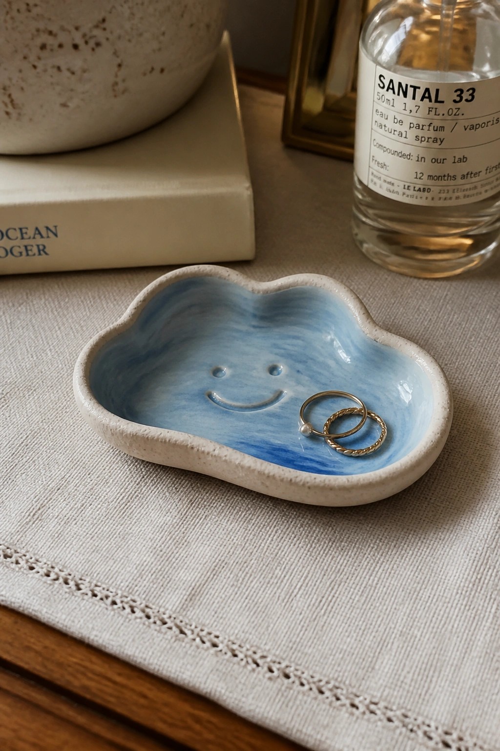 Blue cloud-shaped ceramic dish with smiley face and gold rings on linen