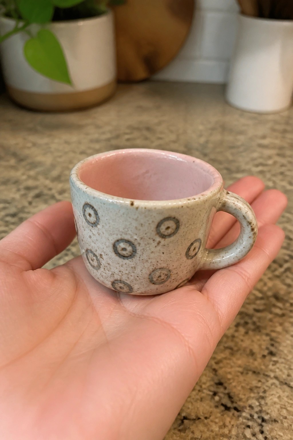 Hand holding small speckled ceramic mug with gray circles and pink interior