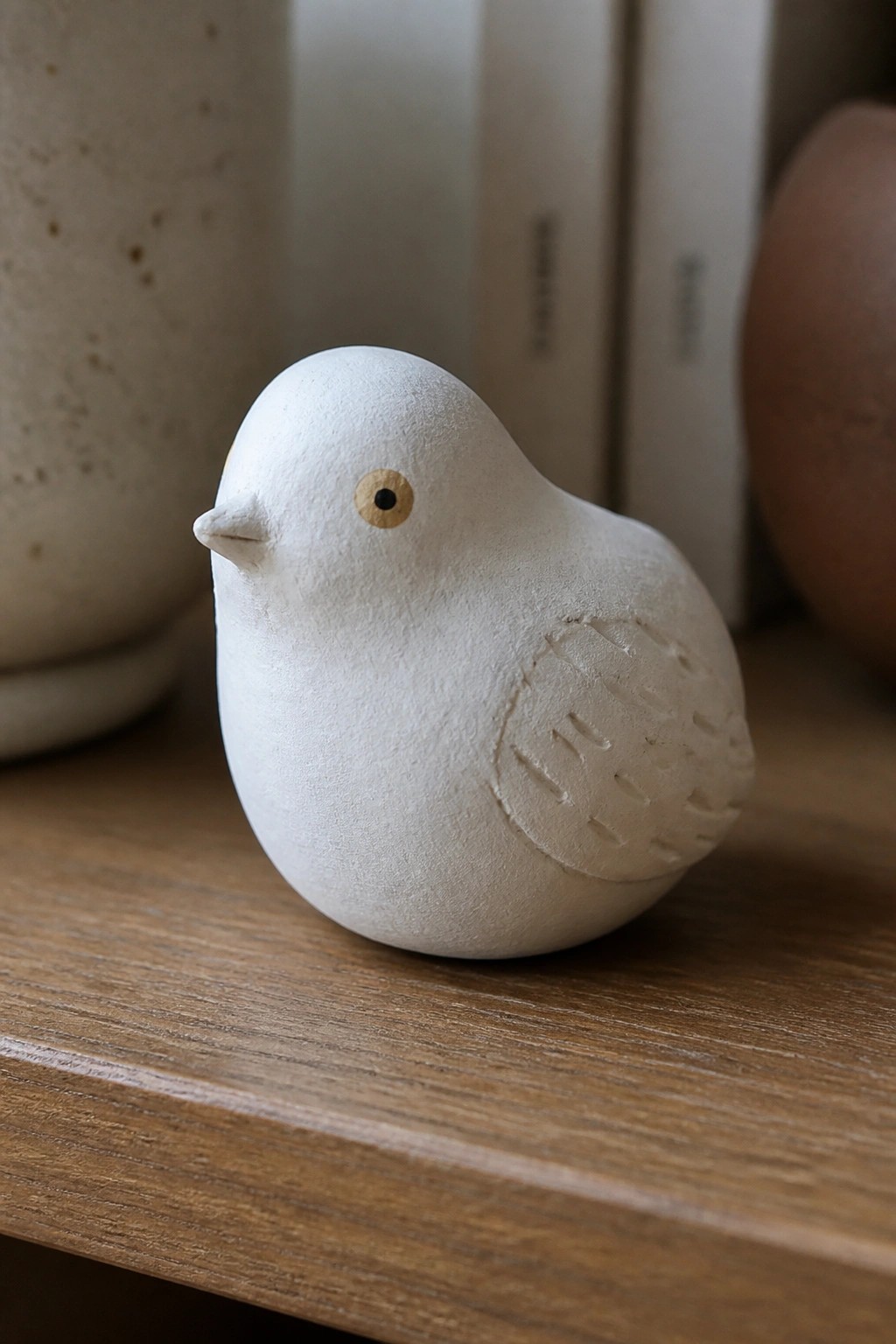 Small white ceramic bird with carved wing on wooden surface.