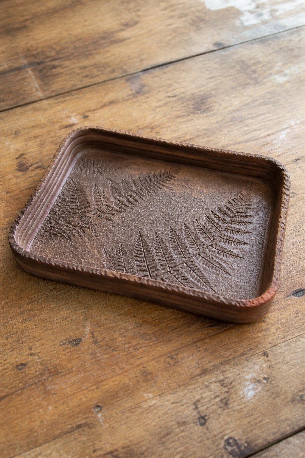 Dark wooden tray with embossed fern leaves on a rustic table surface.
