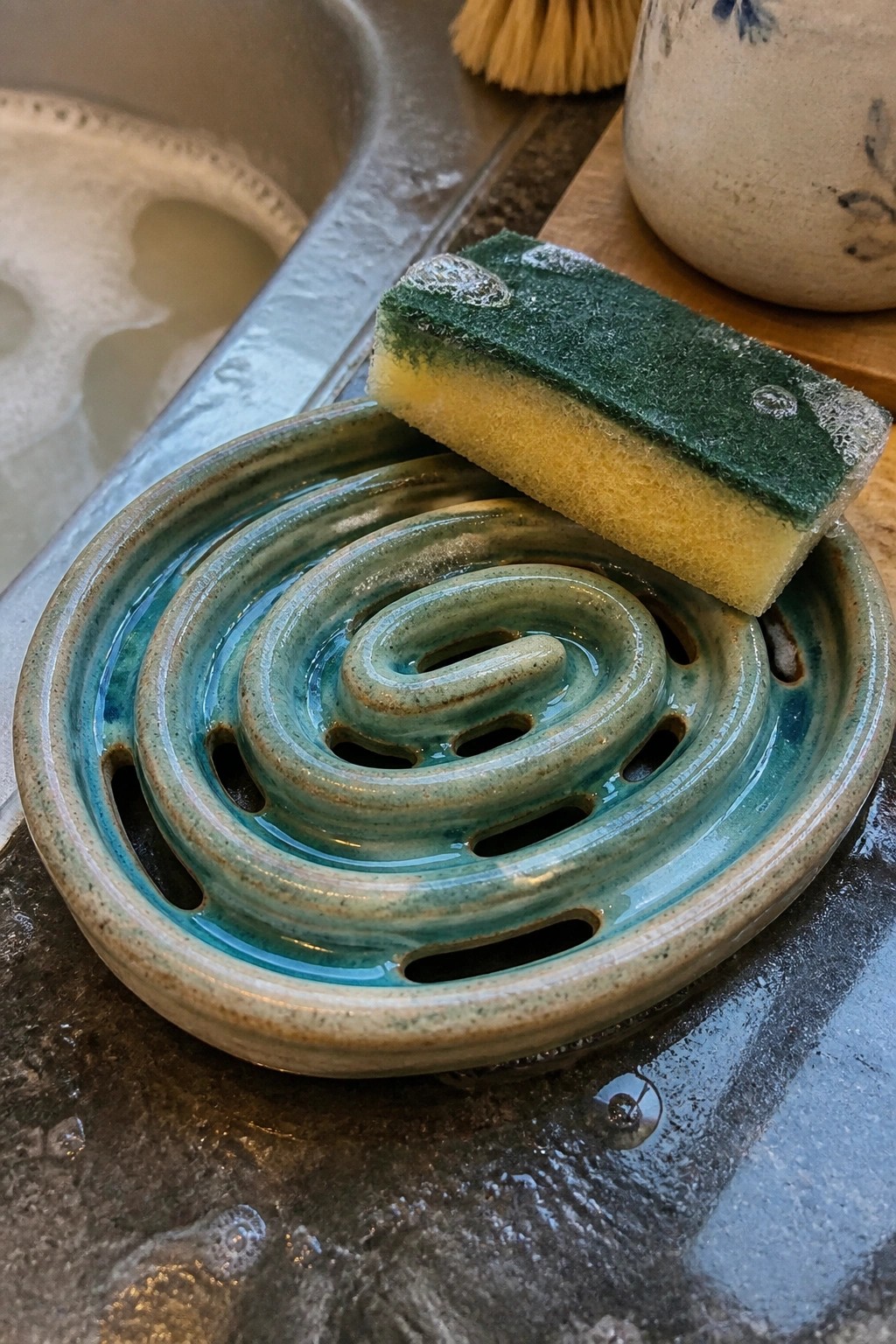 Wet green-yellow sponge on turquoise spiral ceramic dish by soapy sink