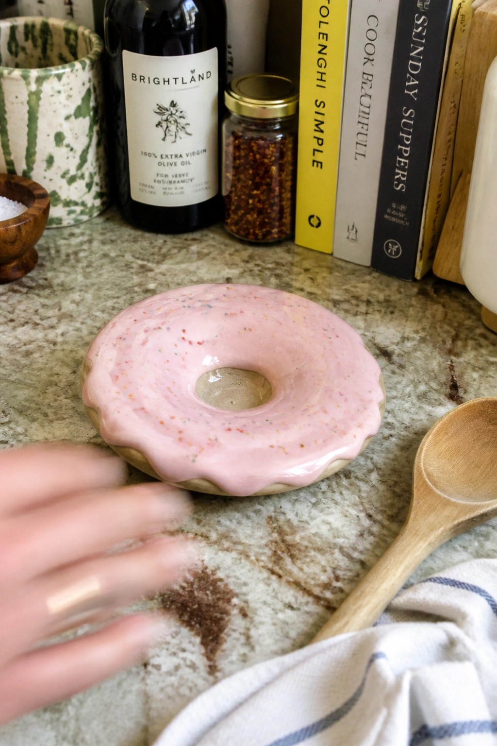 Hand reaching for pink-frosted donut with sprinkles on marble countertop