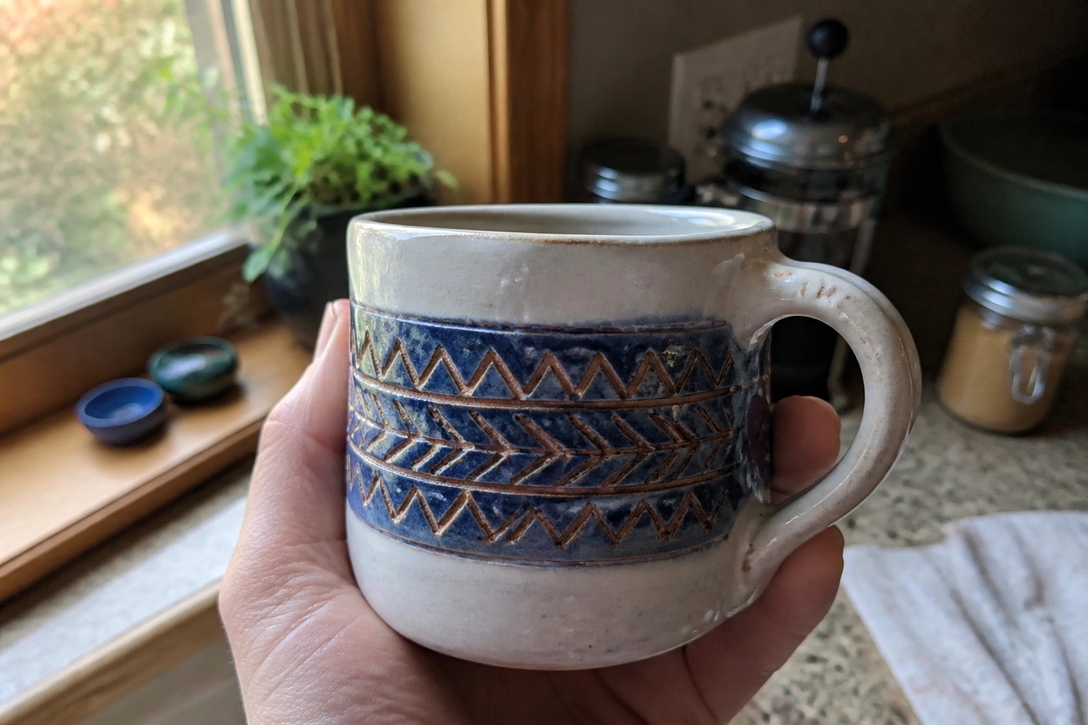 Hand in brown knit sweater holding white mug with blue geometric pattern