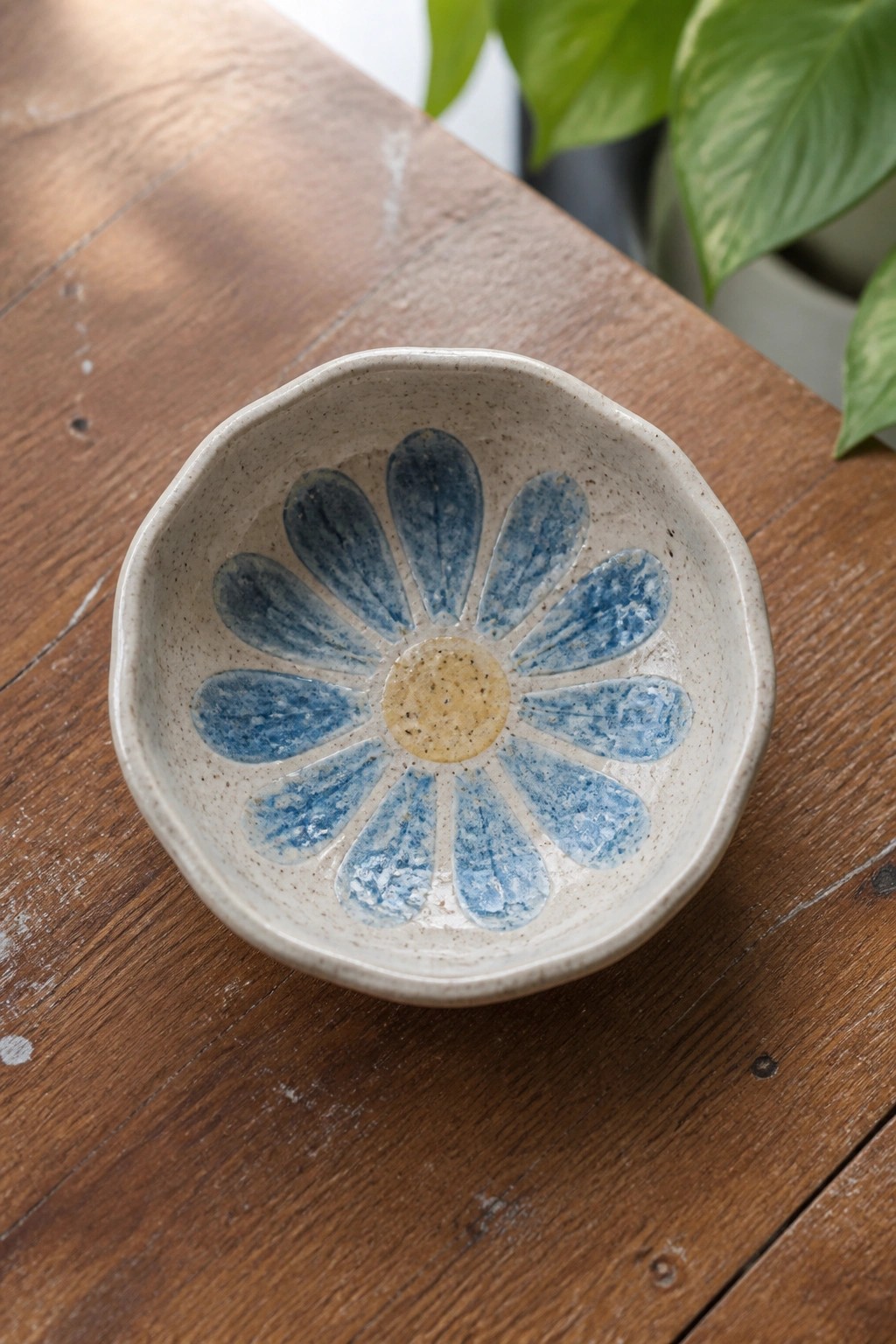 Small ceramic bowl with blue daisy petals and yellow center on wood
