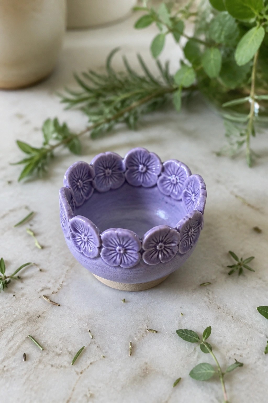 Small purple ceramic bowl with floral rim on marble amid fresh herbs