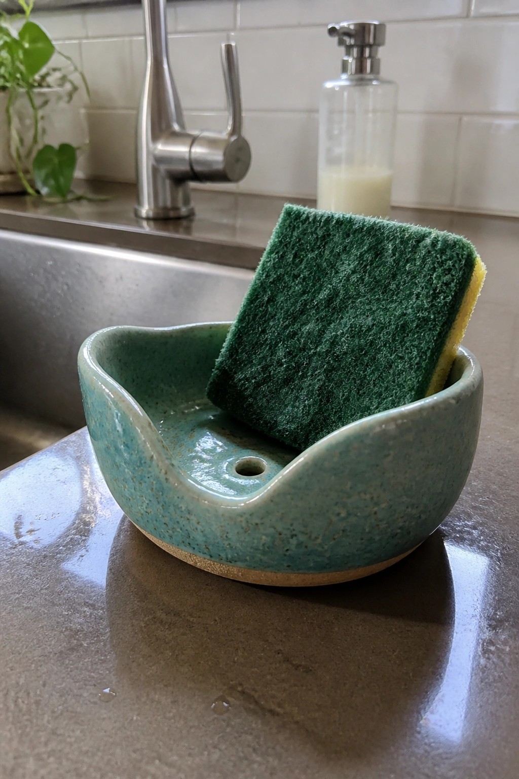 Turquoise ceramic sponge holder with green scrub sponge on kitchen counter
