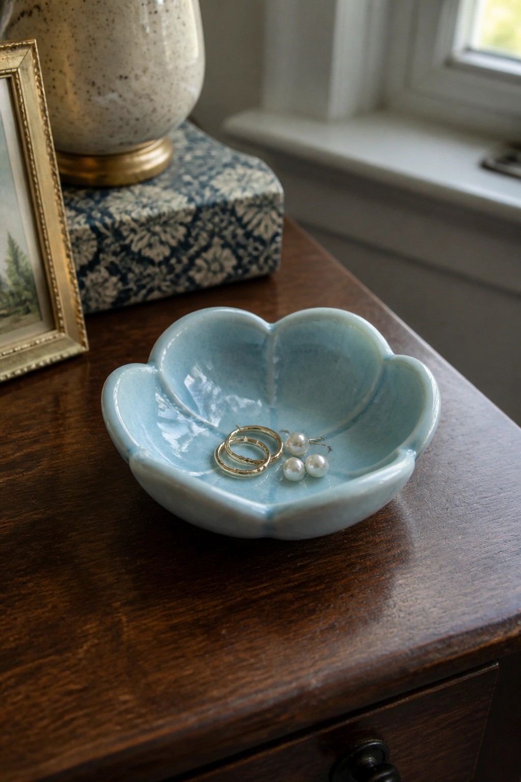 Light blue flower-shaped ceramic bowl with gold hoops and pearls on wooden table