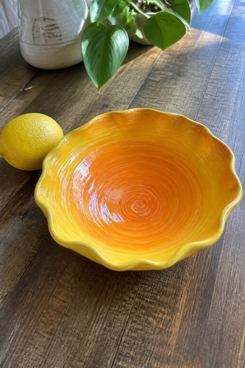 Scalloped yellow-orange ceramic bowl beside lemon on wooden table with plants