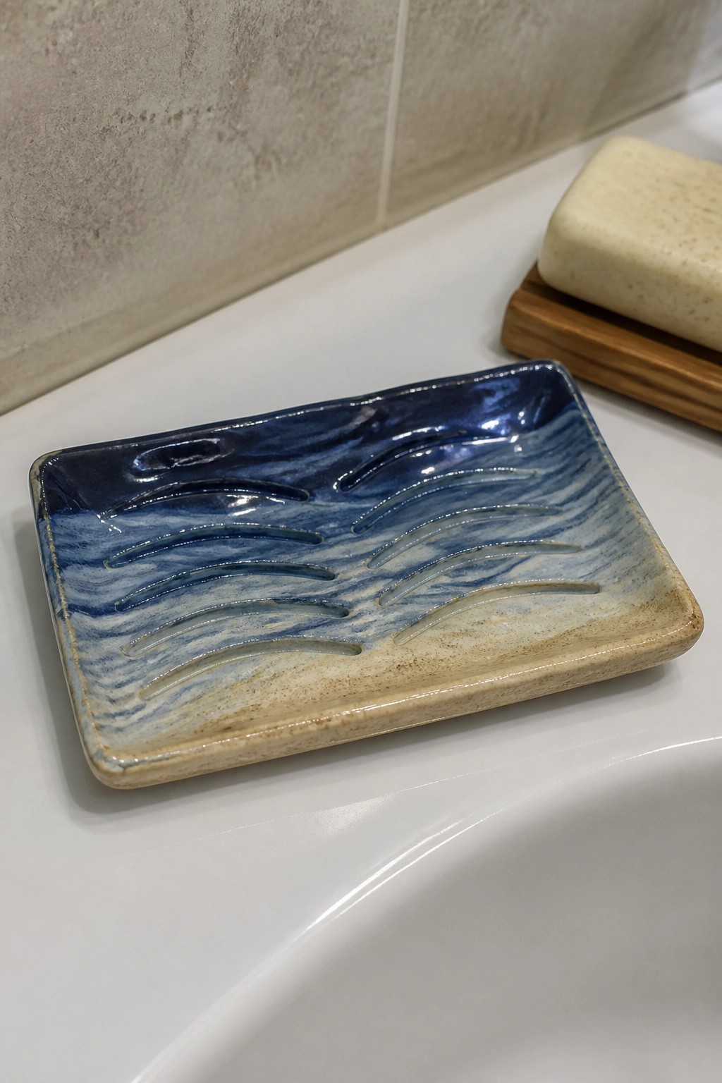 Blue marbled ceramic soap dish with ridges on white sink near wooden soap holder