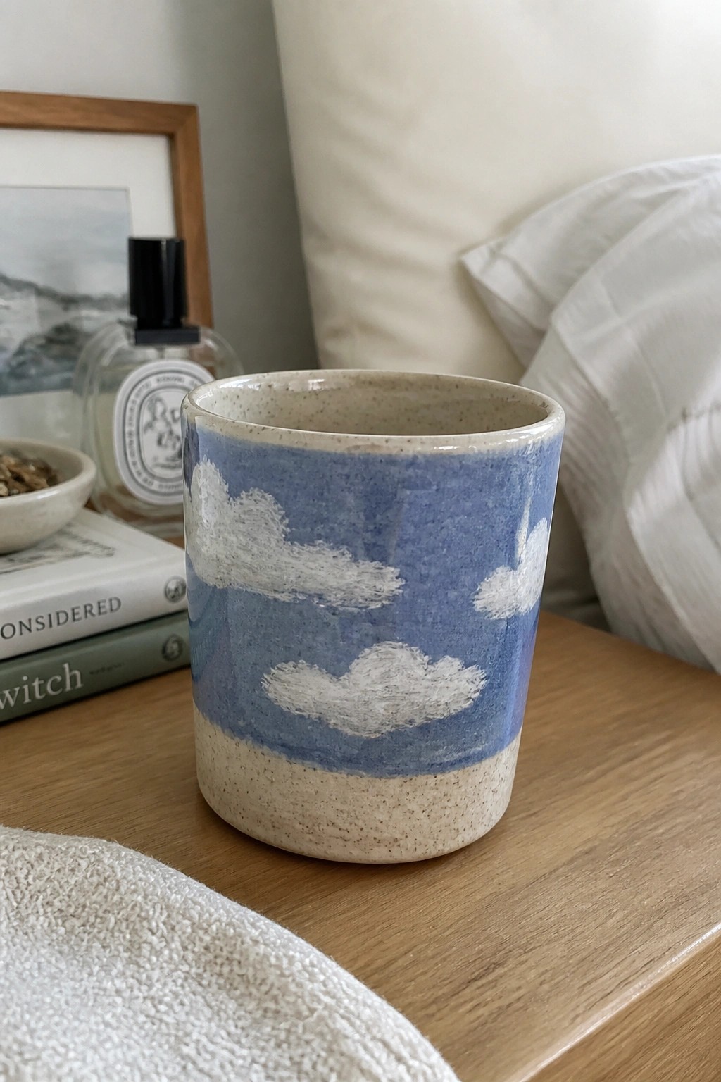 Blue ceramic cup with white clouds on wooden table near books and perfume bottle