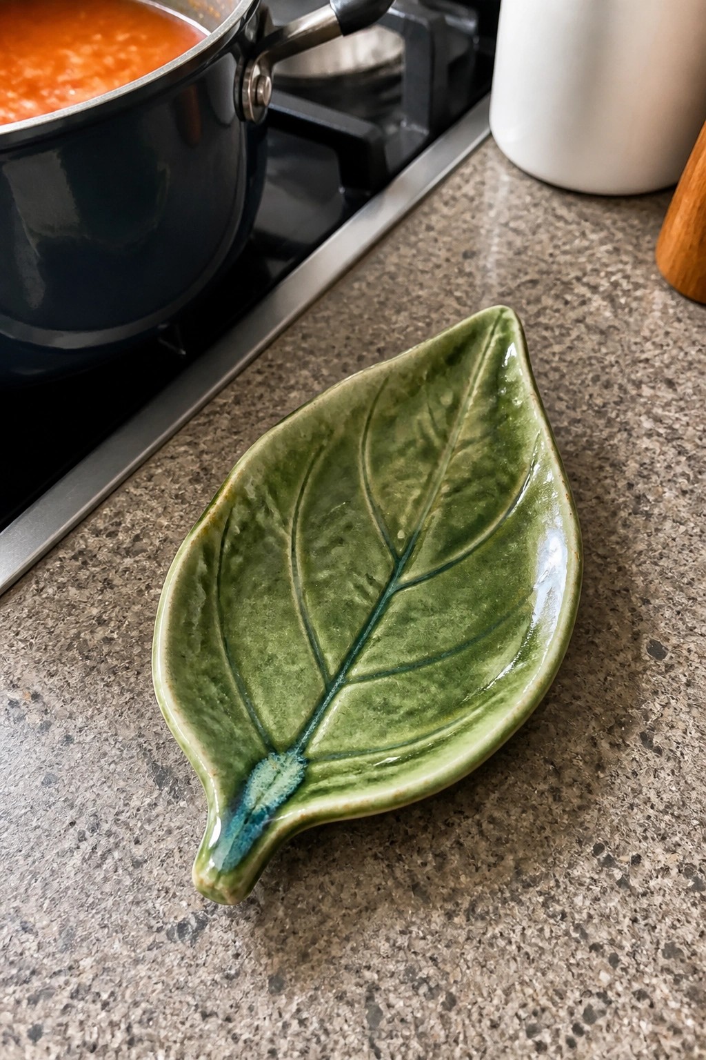 Green ceramic leaf-shaped dish on speckled countertop near pot of orange soup