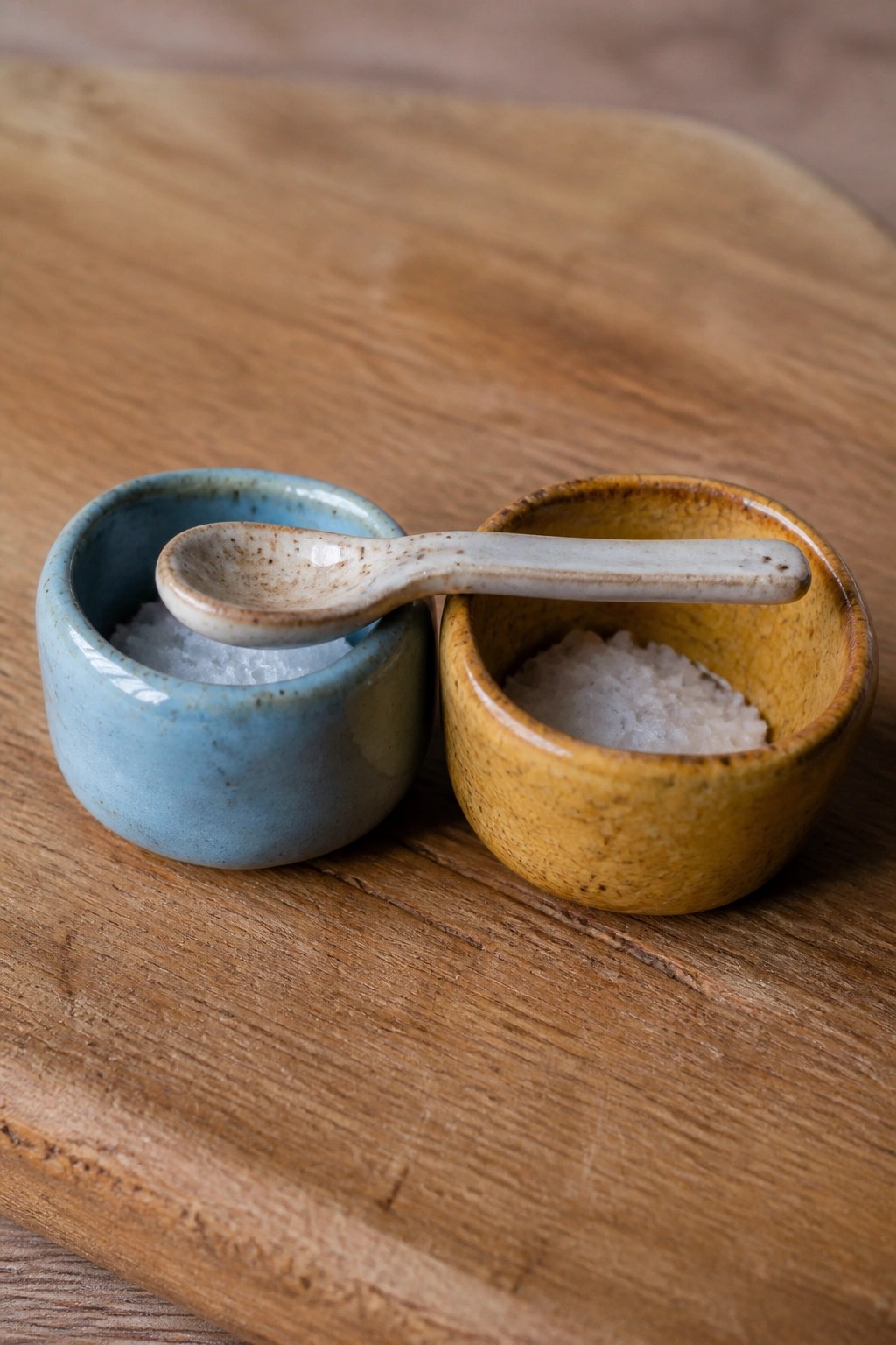 Small blue and yellow ceramic bowls with salt and spoon on wood.