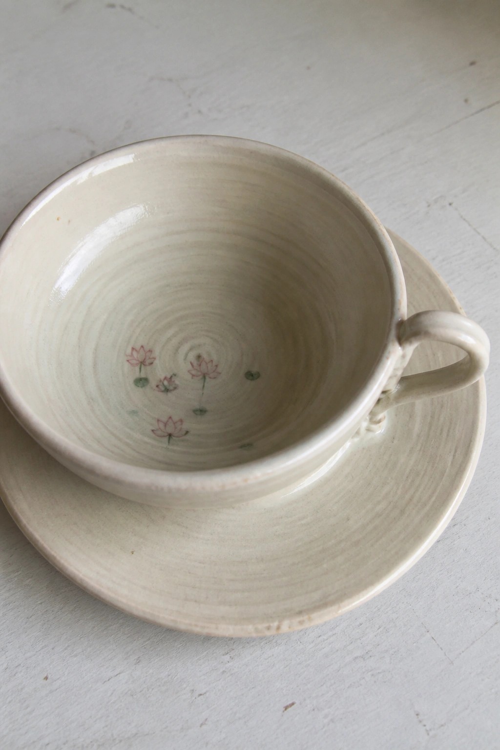 Cream ceramic teacup with pink lotus flowers and green pads on matching saucer