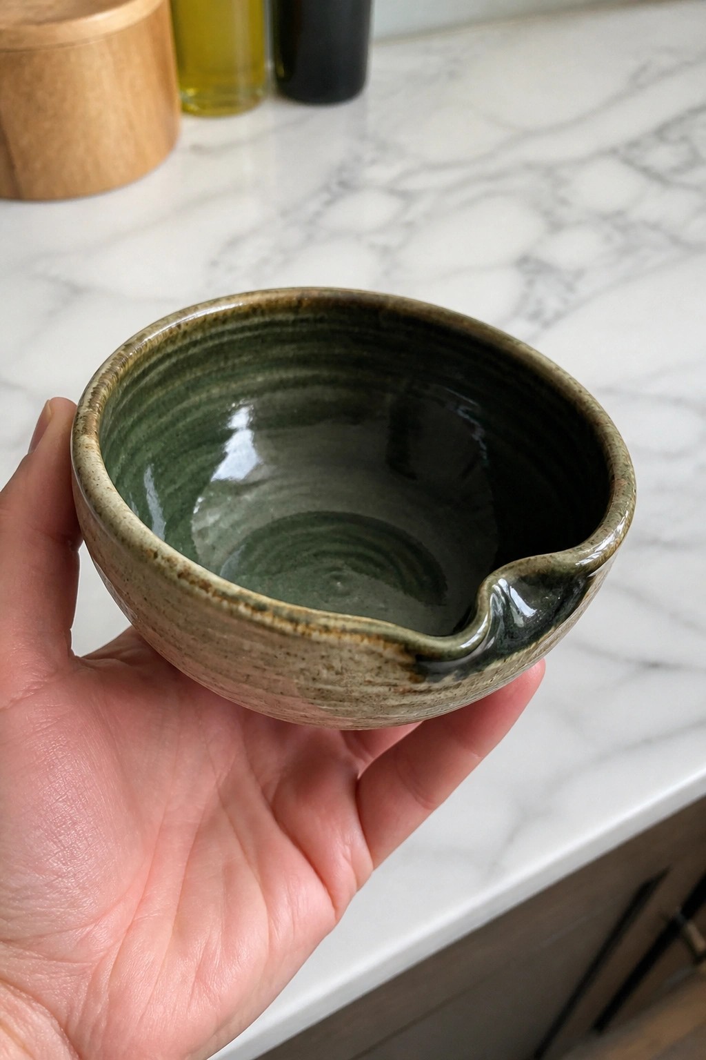 Hand holding green ceramic bowl with spout over marble countertop