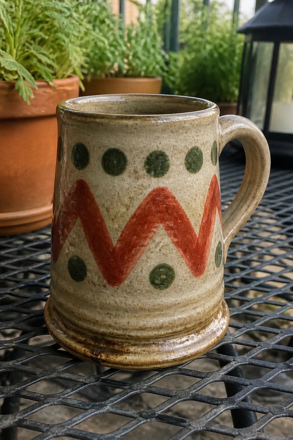 Ceramic mug with red zigzag pattern and green dots on metal table
