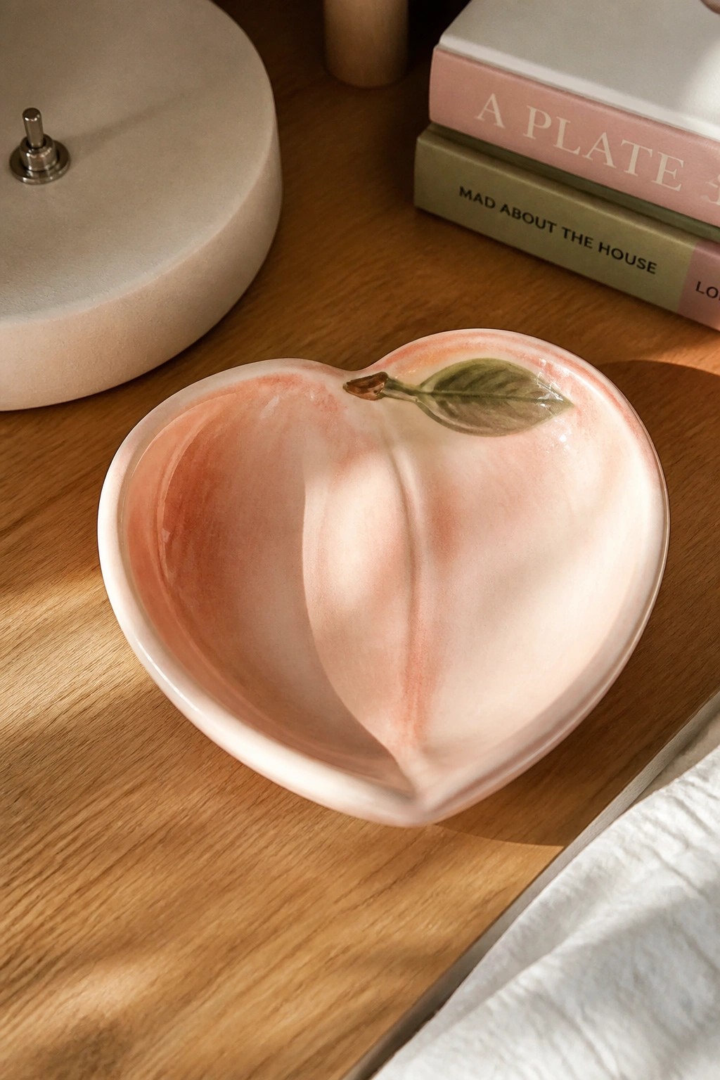 Glossy peach-shaped ceramic bowl in soft pink on wooden table with books.