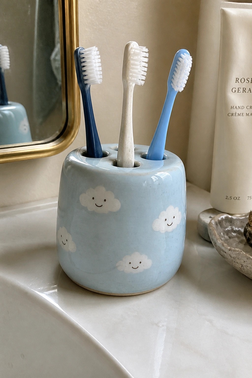Light blue ceramic holder with smiling clouds holding three toothbrushes on bathroom counter