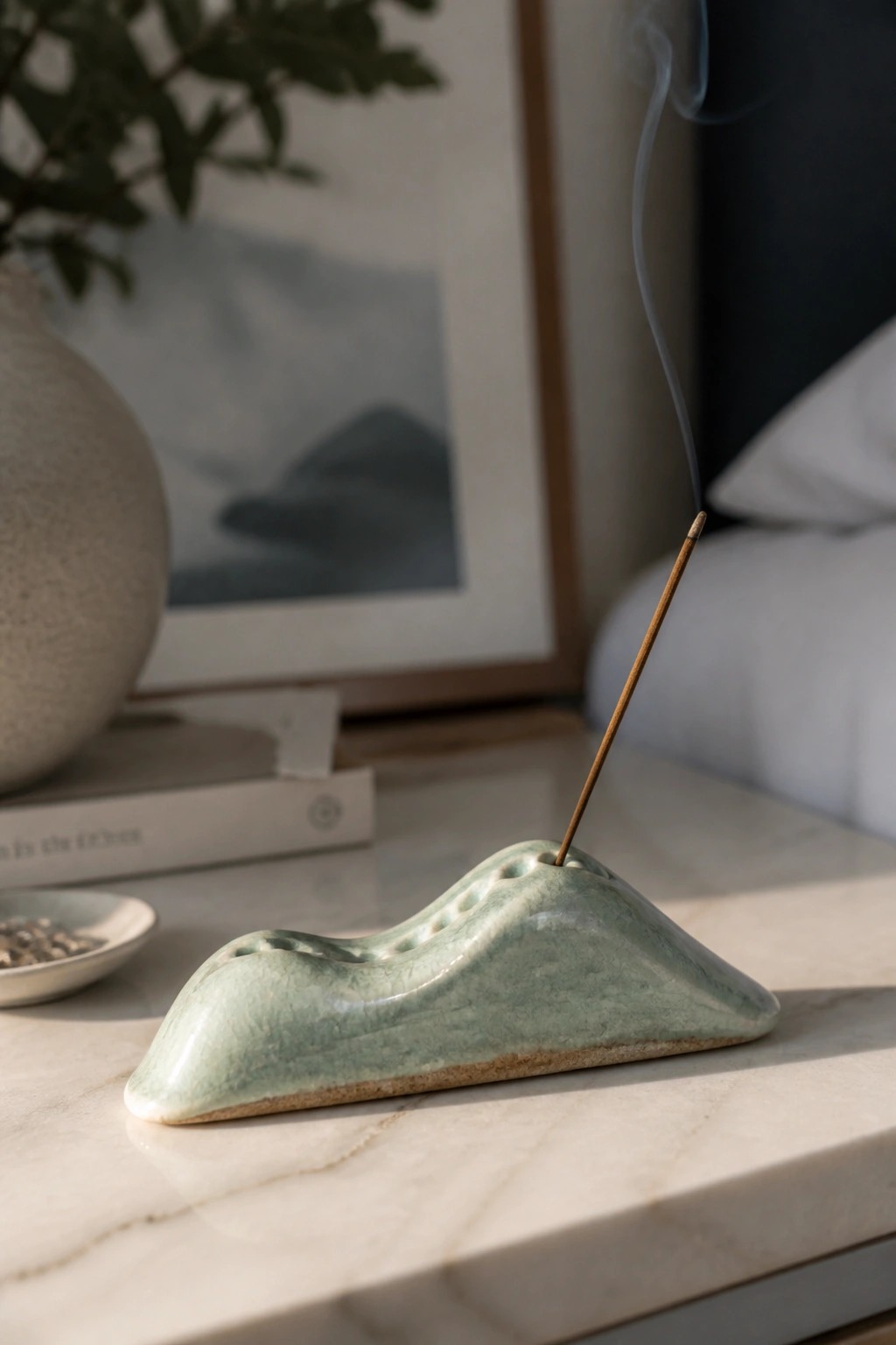 Green ceramic mountain-shaped incense holder with burning stick emitting smoke on marble.