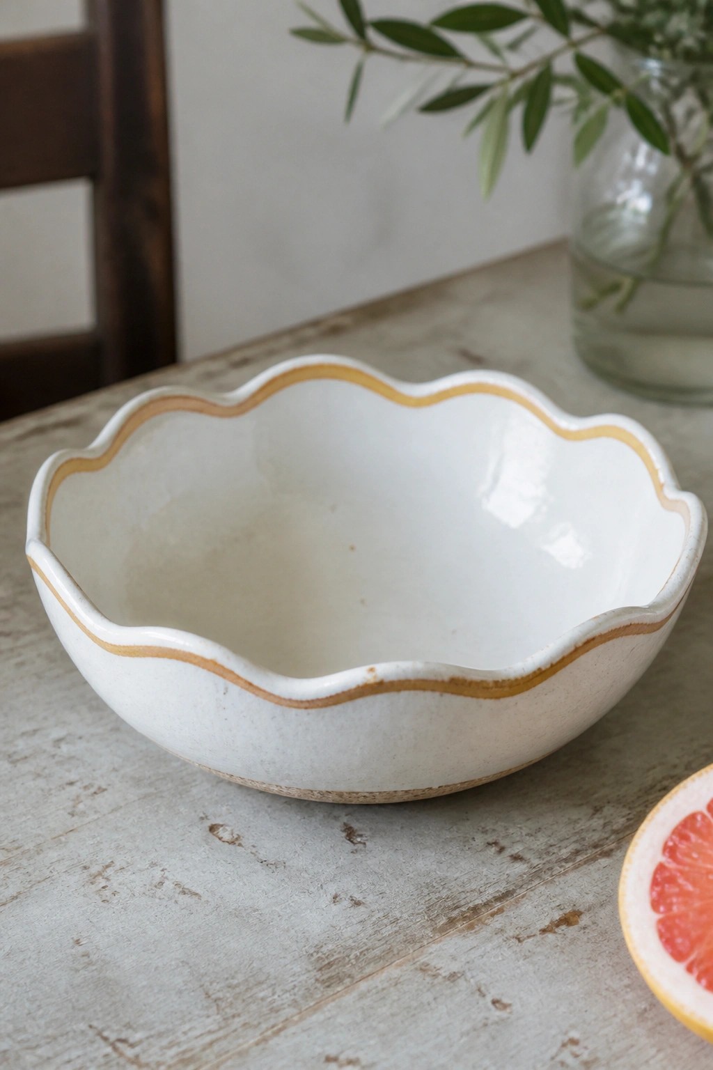 White scalloped ceramic bowl with brown rim on wooden table beside grapefruit half.