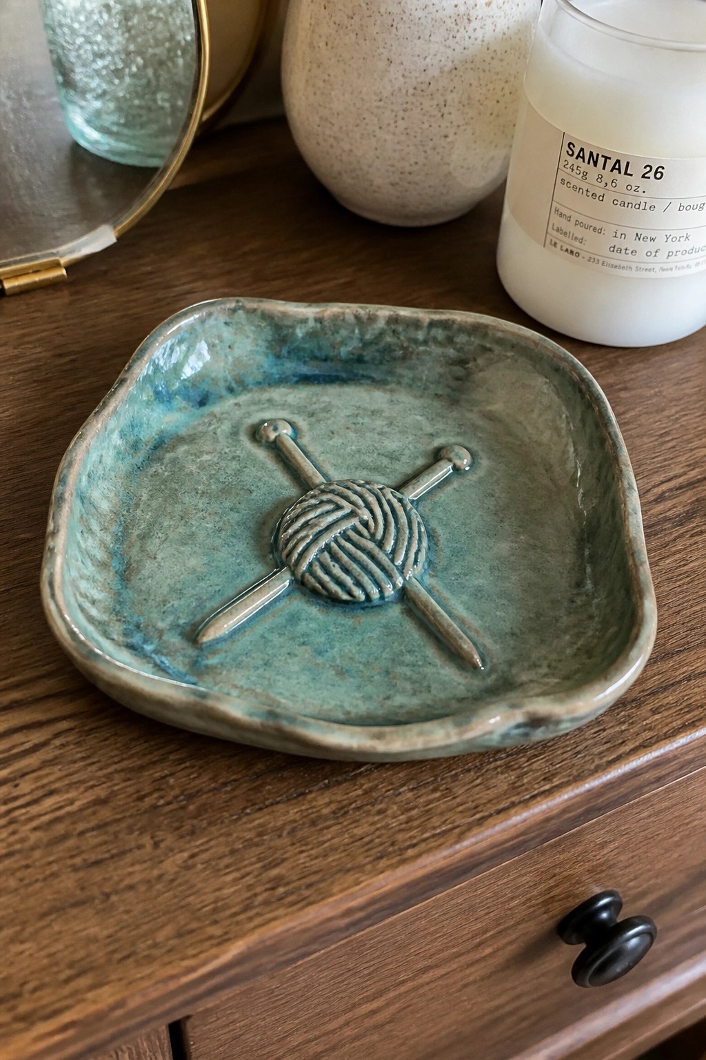 Teal ceramic dish with knitting needles and yarn design on wooden table