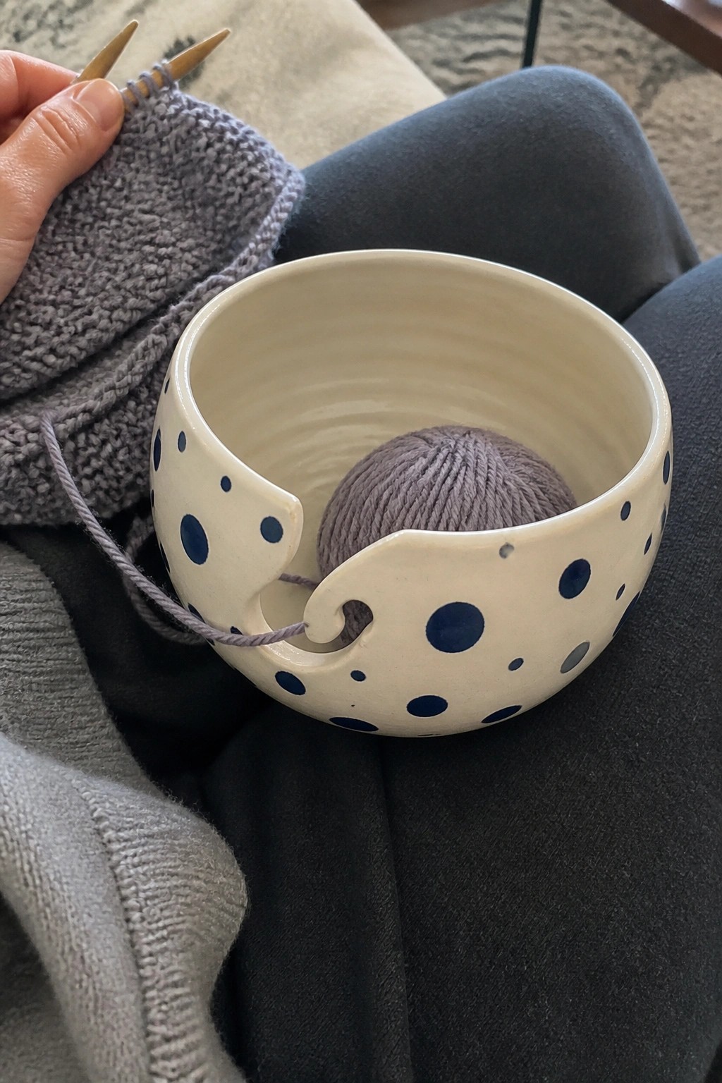 Hands knitting gray yarn from blue polka dot ceramic bowl on lap