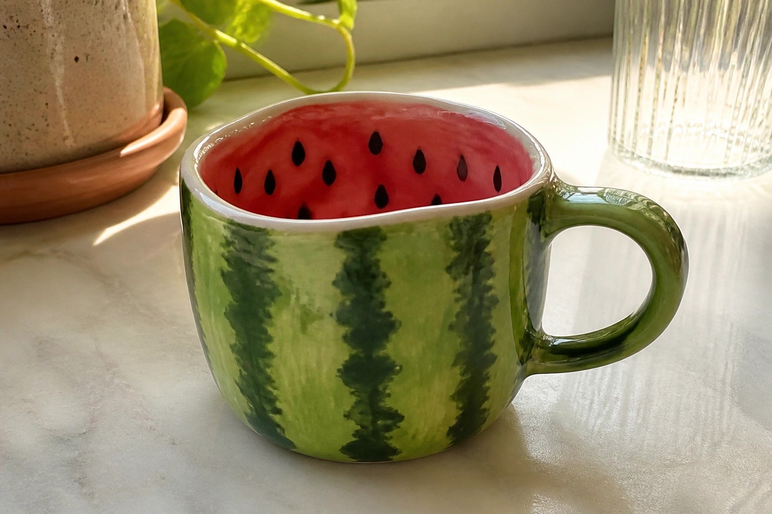Watermelon-themed ceramic mug with green striped exterior and pink seeded interior on counter