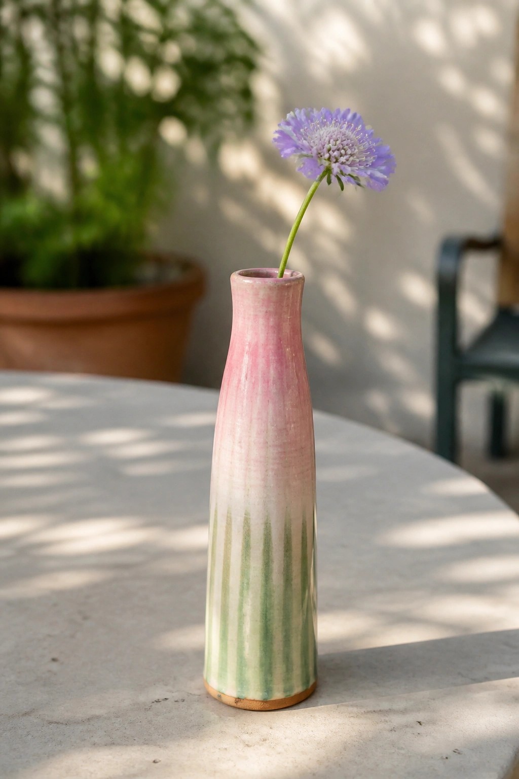 Pink and green striped ceramic vase with purple flower on white table