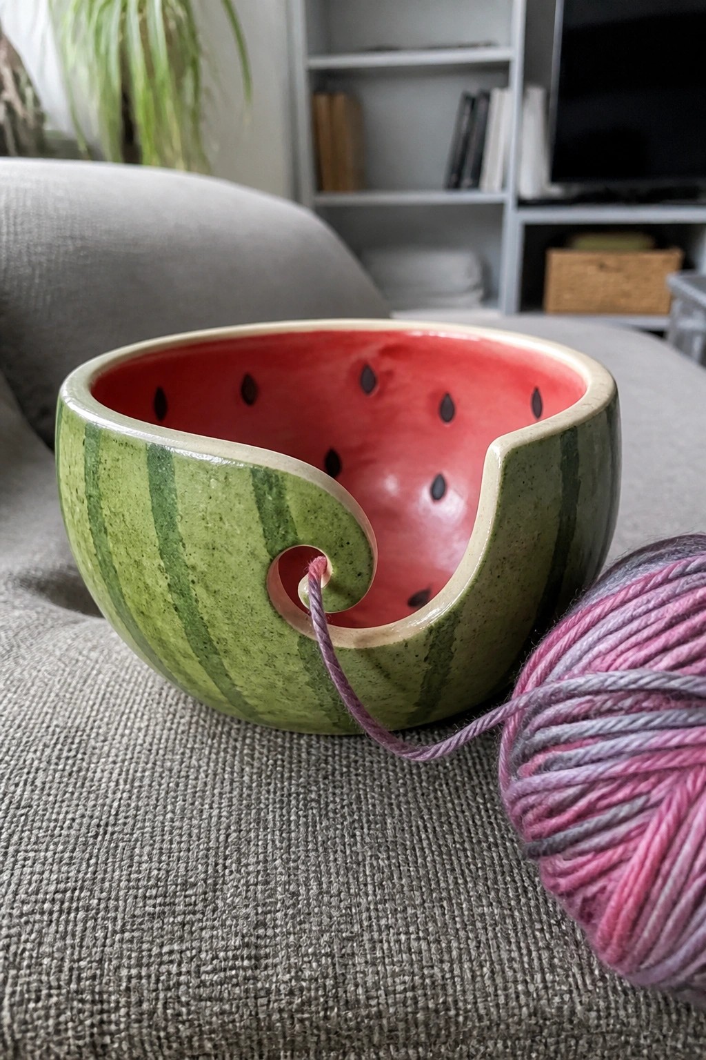 Watermelon ceramic yarn bowl with pink-purple yarn on gray couch