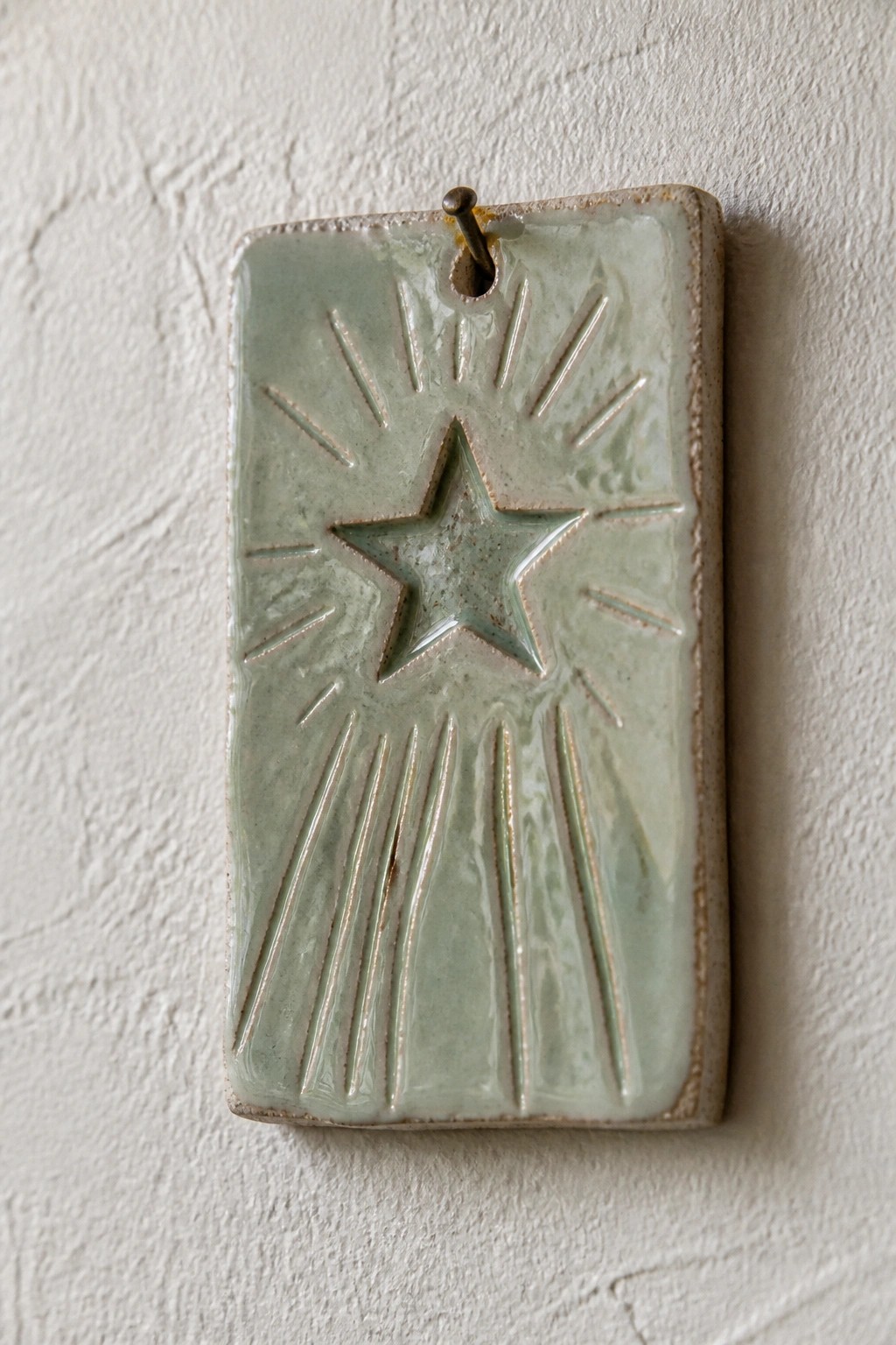 Pale green rectangular ceramic tile with raised star and rays on white wall