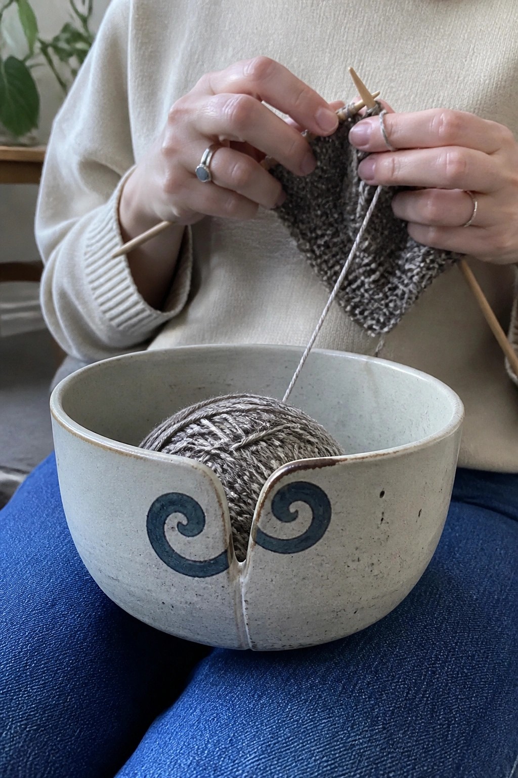 Hands knitting gray yarn from a blue-swirled ceramic bowl resting on lap