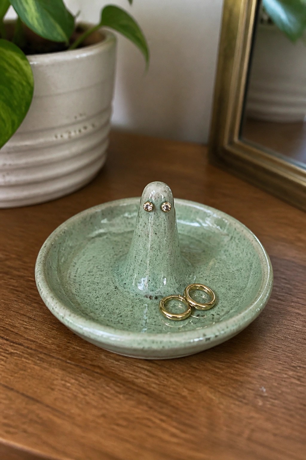 Green ghost-shaped ceramic dish holding two gold rings on wooden table