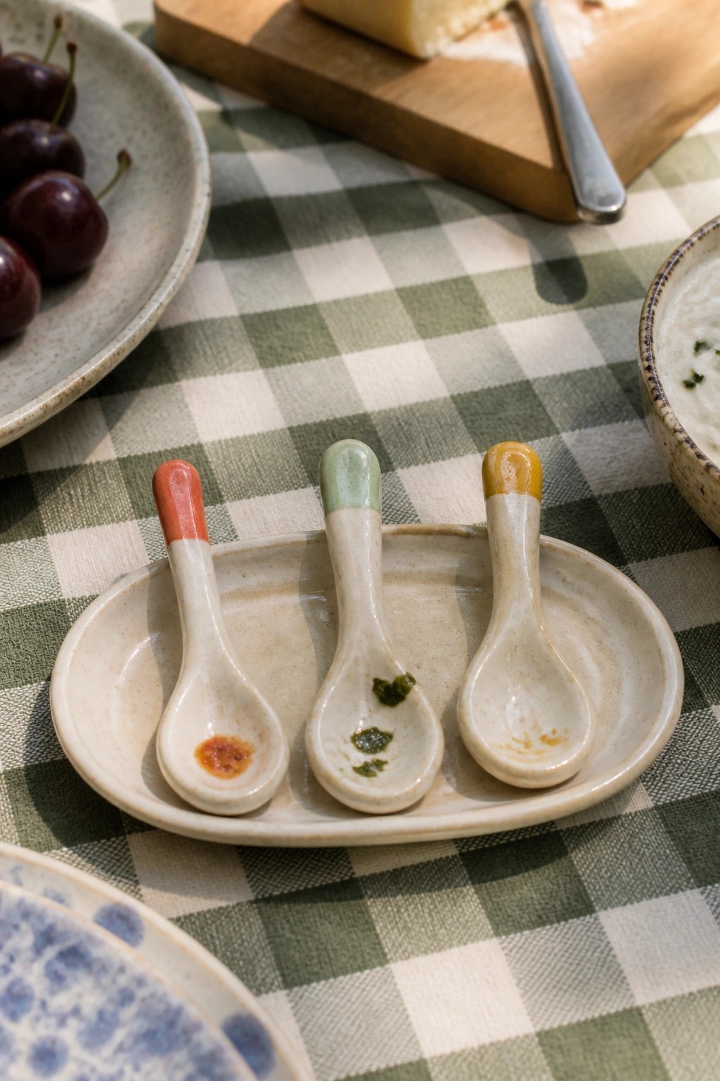 Three ceramic spoons with red, green, and yellow tips on a plate over gingham cloth