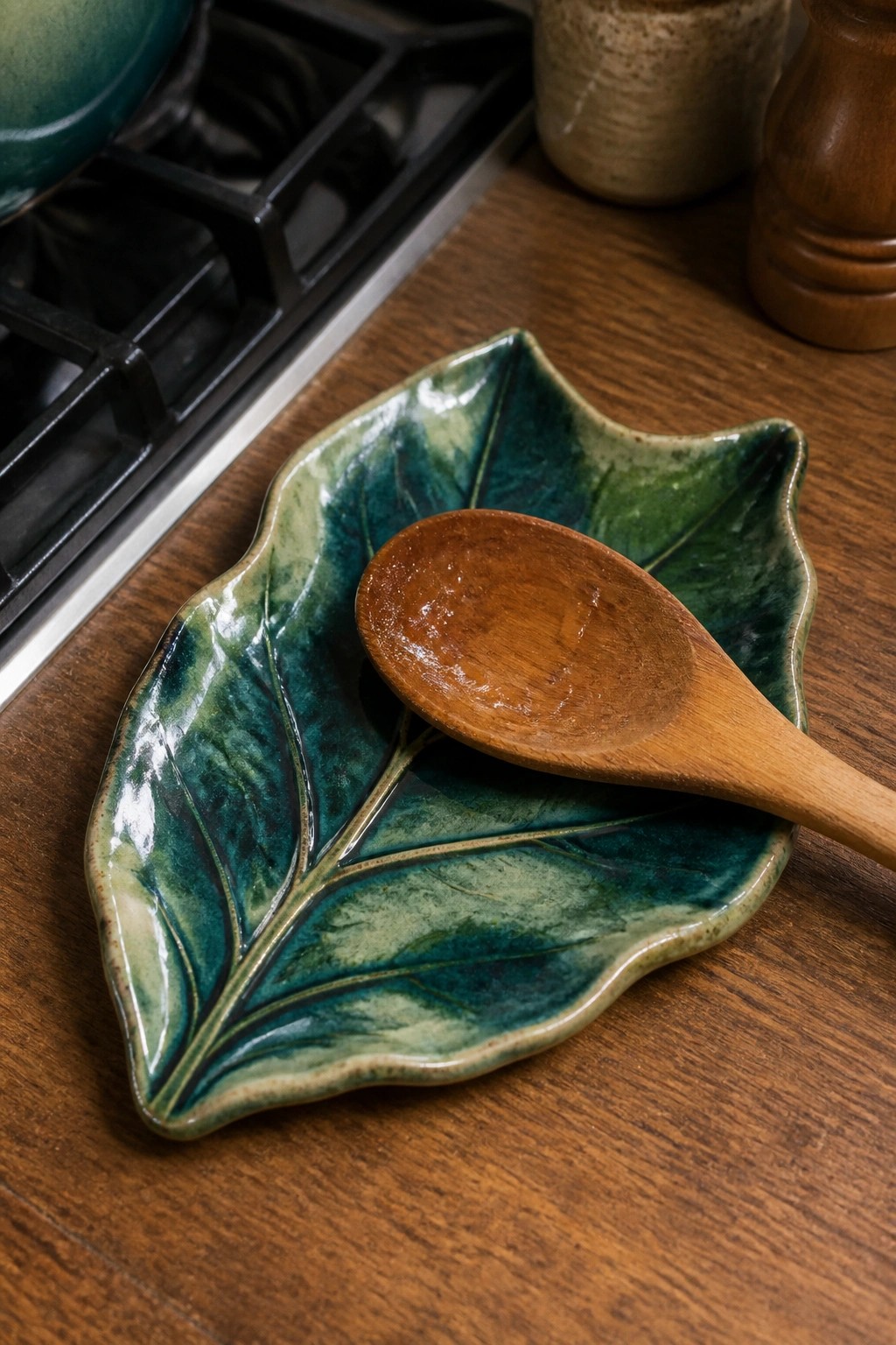 Wooden spoon on glossy green-blue leaf-shaped ceramic dish on wooden counter