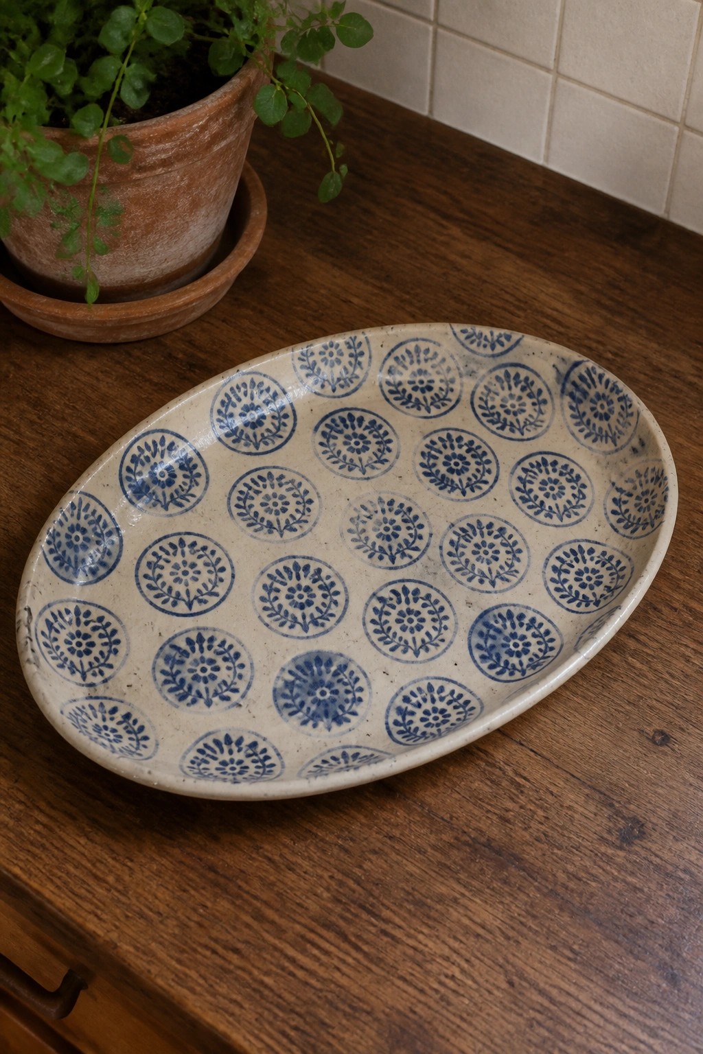 Oval ceramic platter with blue floral patterns on wooden table beside potted plant