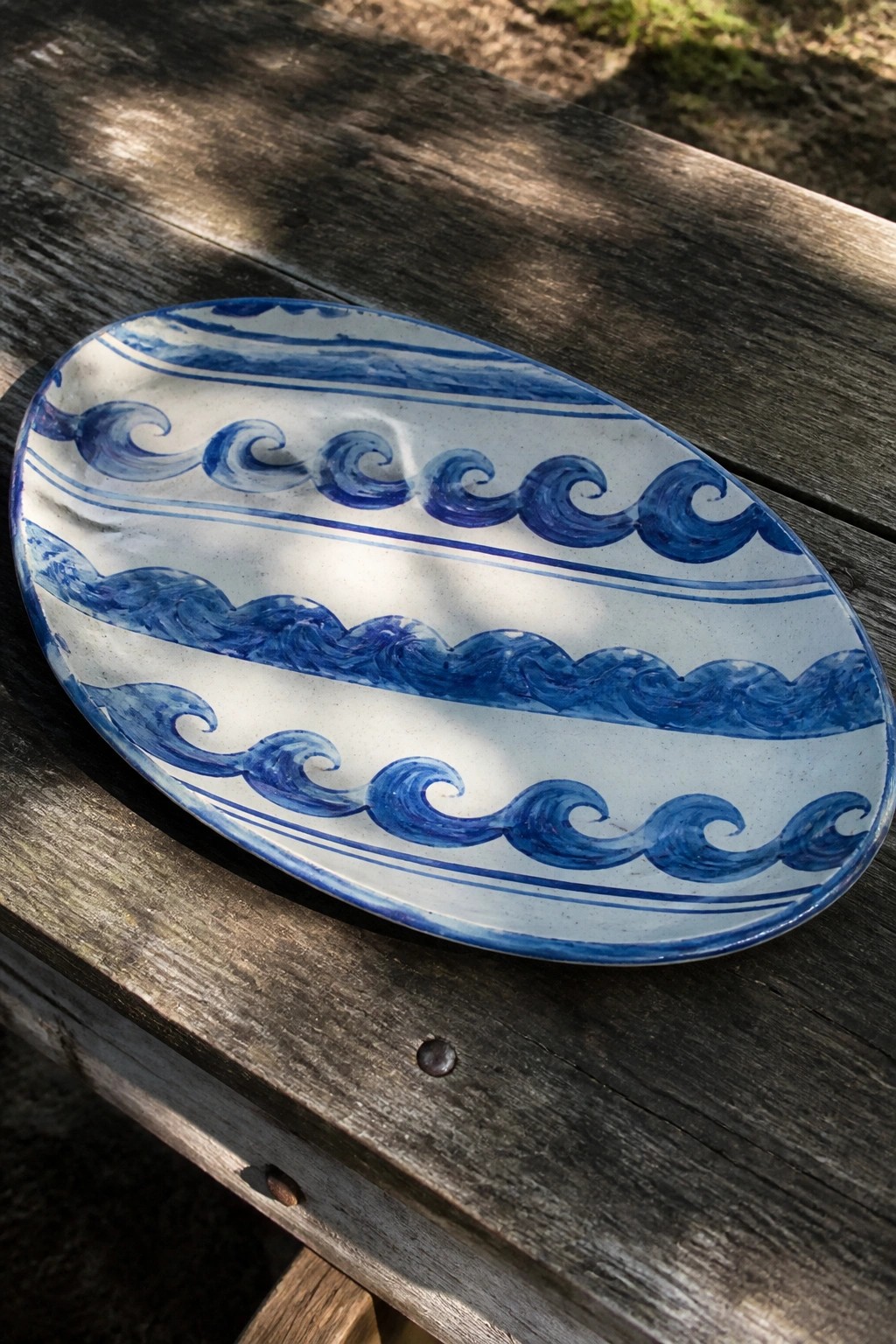 Oval white ceramic plate with blue wave patterns on wooden table
