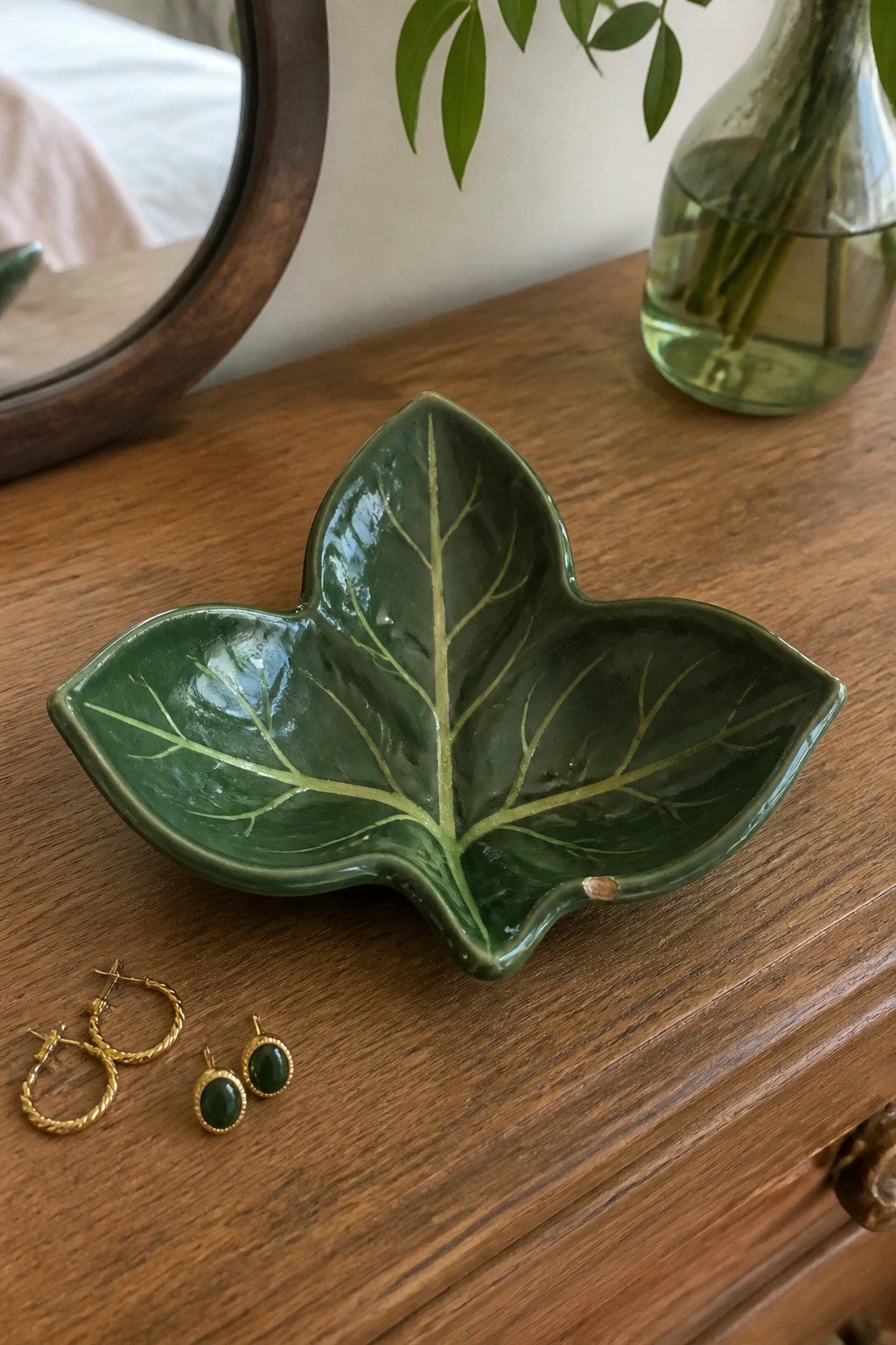 Green ceramic leaf bowl with gold hoop and green stud earrings on wood