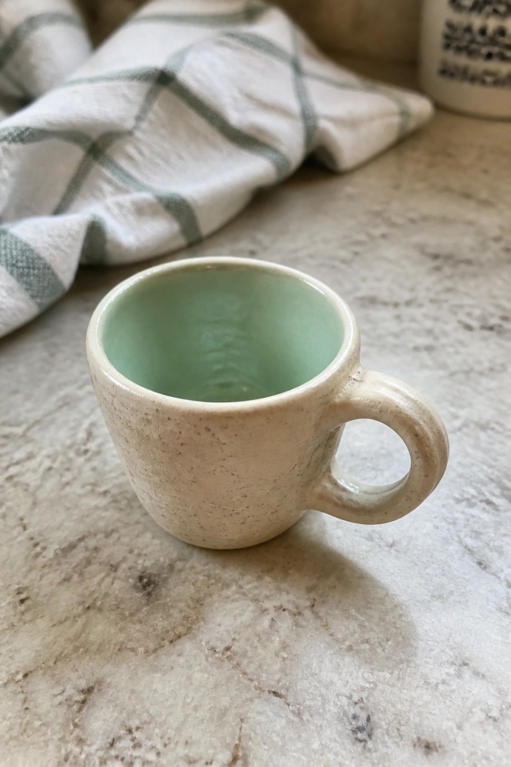 Small speckled beige ceramic mug with mint green interior on marble counter