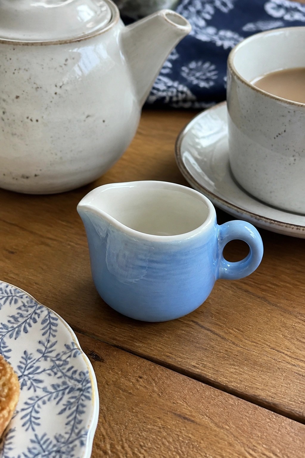 Blue creamer jug beside white teapot and cup on wooden table