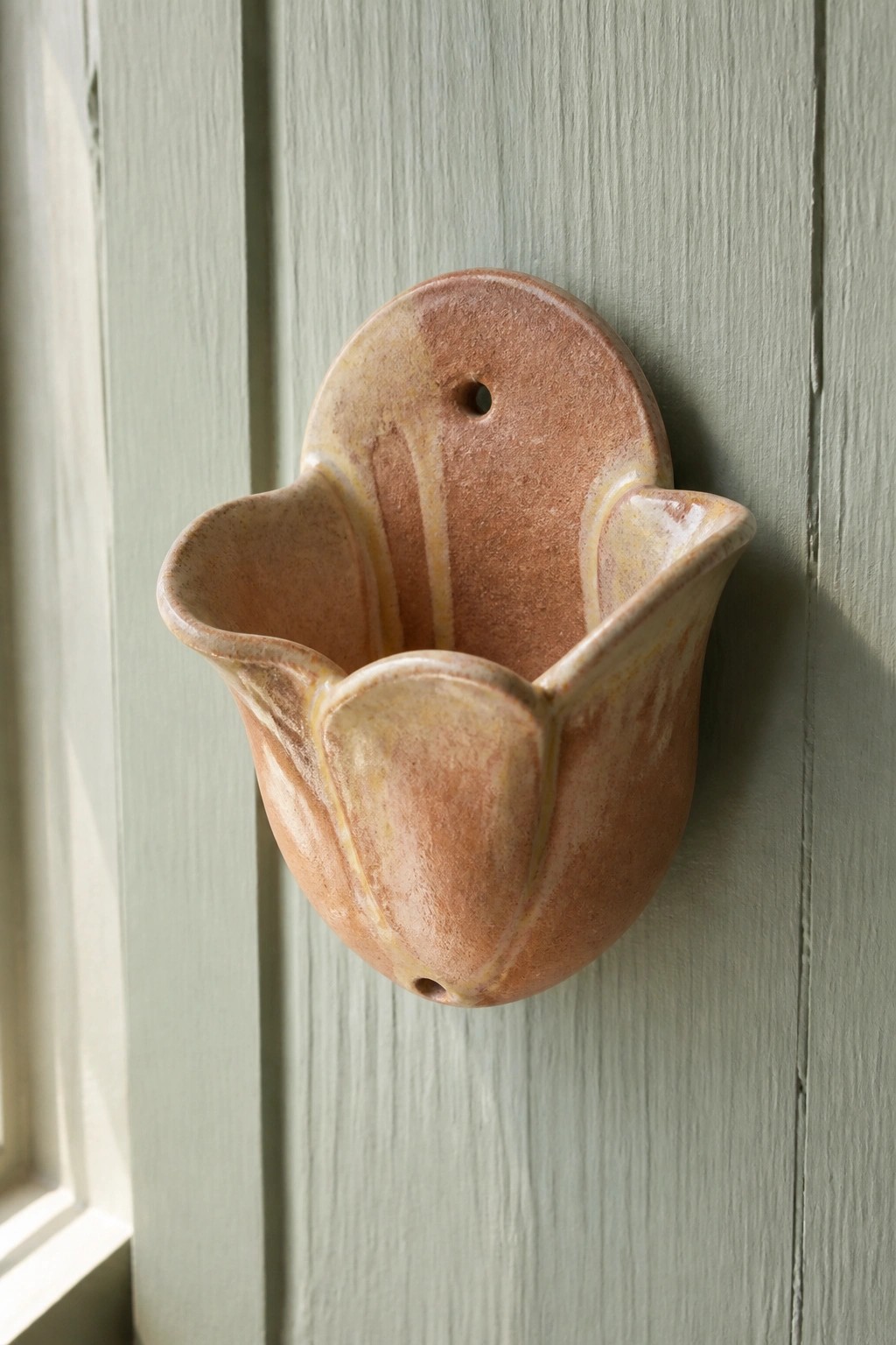 Ceramic tulip-shaped wall pocket with petal edges, hanging hole on the back plate, and drainage hole at the bottom, mounted on green wood.
