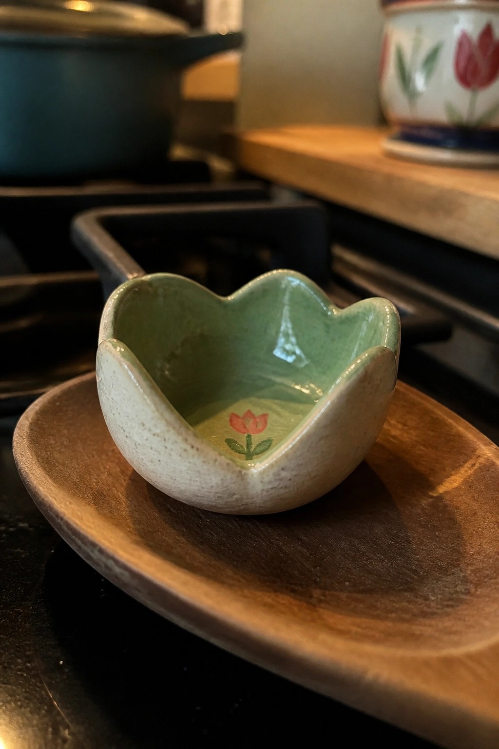 Small ceramic bowl with green glaze and pink tulip on wooden dish