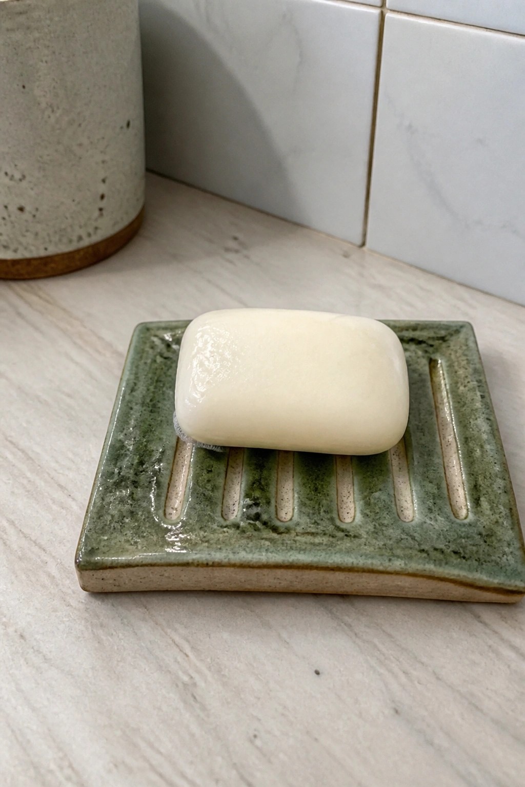 White soap bar on green ceramic dish with ridges on marble counter